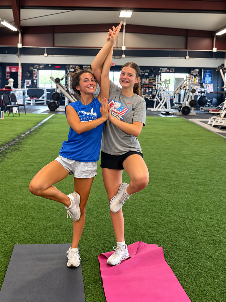 Two young athletes balancing in tree pose on turf